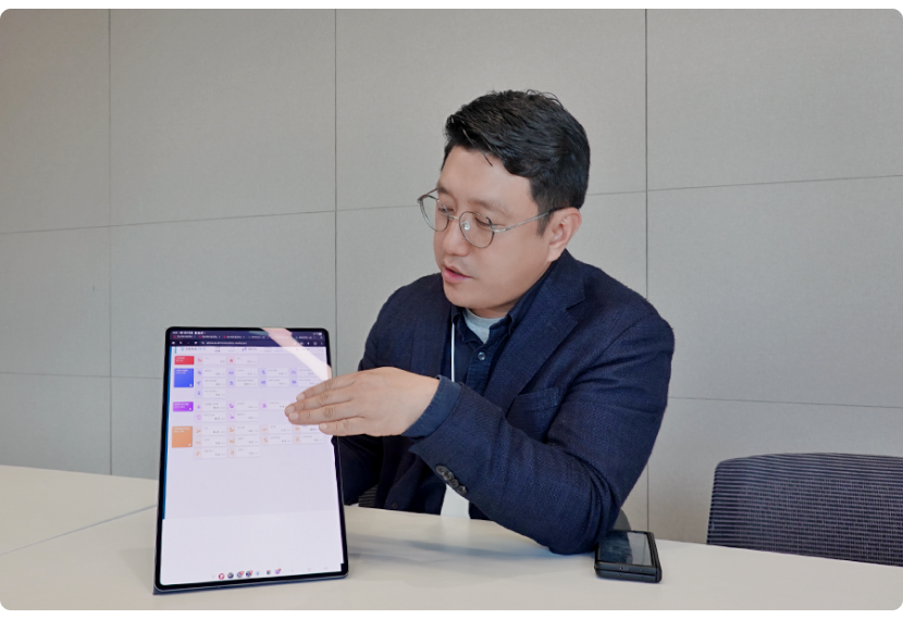 에스앤아이 코퍼레이션 김민수 팀장이 테이블에 앉아 태블릿 화면을 보여주며 인터뷰하는 모습
